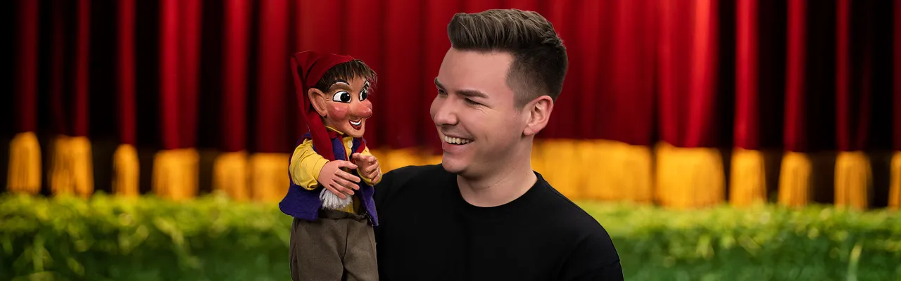 Raphael Kovarik, der Gründer der Kasperlkiste, steht mit dem Kasperl vor dem Vorhang. Die beiden sehen sich in die Augen und lächeln.