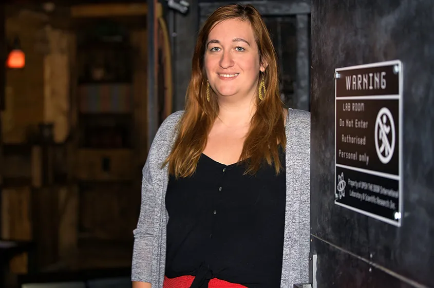 Ulrike Dziurzynski zeigt uns einen ihrer Escape Rooms namens "Der Schatz des Kolumbus". Sie lehnt an der Eingangstür, zu sehen ist auch ein Warnschild.