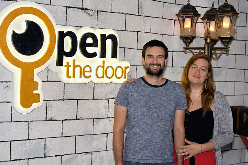 Ulrike Dziurzynski und ihr Mann Filip vor dem Logo ihres Escape Rooms "Open The Door"