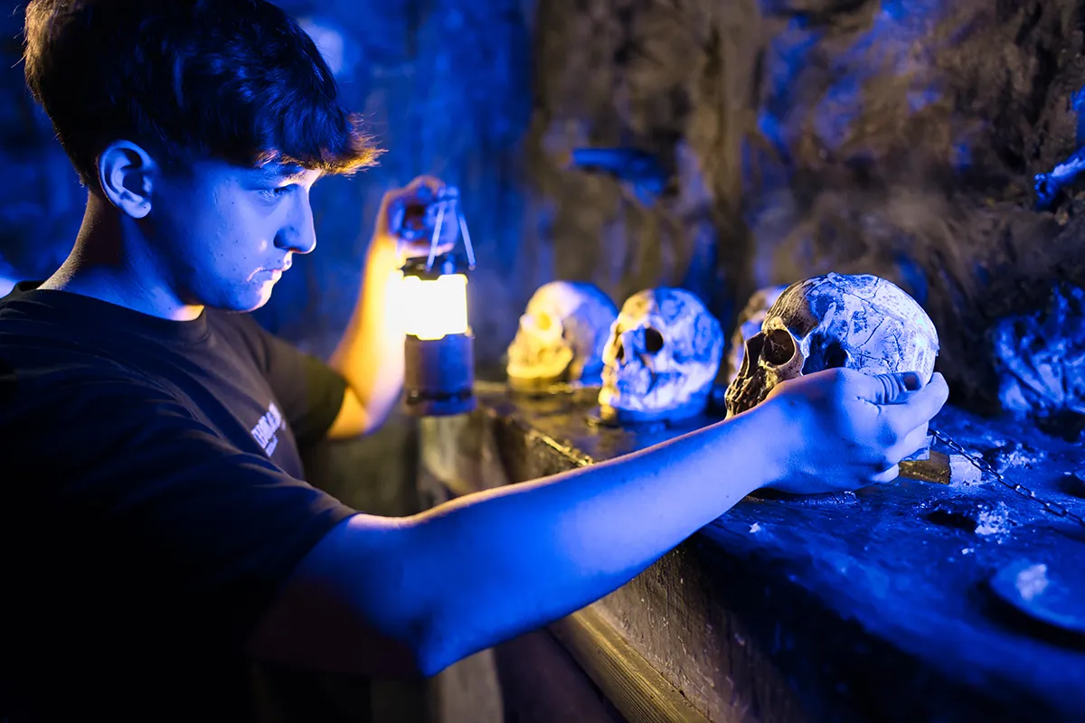 Eine Szene im Escape Room "Open The Door" in Wien: Ein junger Mann betrachtet einen Totenkopf und nimmt dabei eine Lampe zur Hilfe.